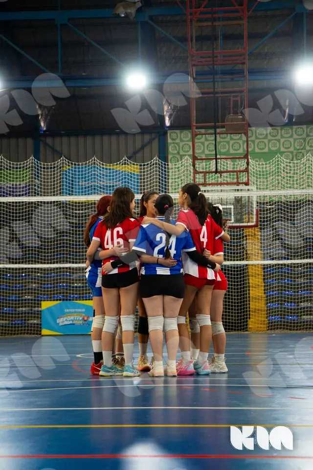 Jugadoras de rojo y azul reunidas en un abrazo en la cancha.